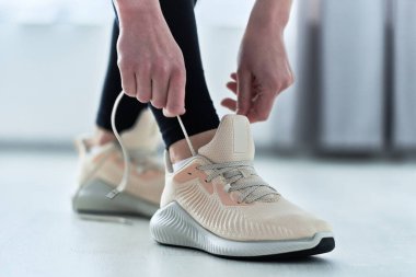 Spor salonundaki kadın ayakkabı bağcıklarını bej, rahat spor ayakkabılara bağlıyor ve koşuya ve antrenmana hazırlanıyor. Spor yap ve formda ol. Sportif yaşam tarzı olan spor insanları.    