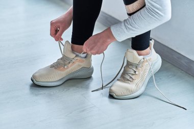 Atletik kadın ayakkabı bağcıklarını bej renkli rahat spor ayakkabılara bağlıyor ve koşuya ve koşuya hazırlanıyor. Spor yap ve formda ol. Sportif yaşam tarzı olan spor insanları. 