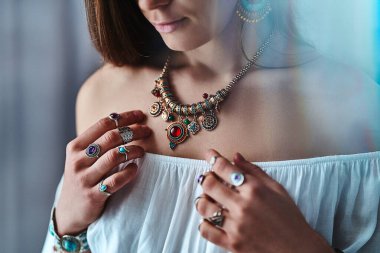 Beyaz bluz giyen, altın büyük kolyeli, taşlı gümüş yüzüklü şık bir kadın. Mücevher aksesuarlarıyla süslü moda Hintli hippi çingene kıyafeti. 