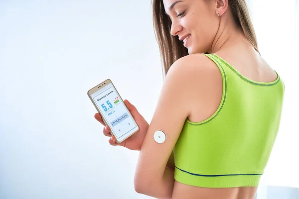 Diabetics patient checking glucose level with a remote sensor and smartphone. Continuous monitoring glucose levels without blood using digital glucose meter. Technology in diabetes treatment and diabetic lifestyle