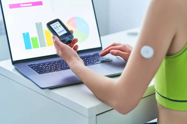 Diabetic patient using remote sensor and computer for online monitoring and examining glucose blood levels graphs. Medical technology in diabetes treatment, healthcare