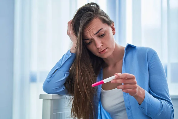 Sad upset unhappy woman holds pregnancy test