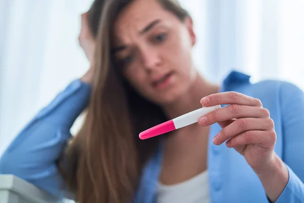 Shocked surprised woman holds pregnancy test with positive result. Unplanned and unwanted pregnancy