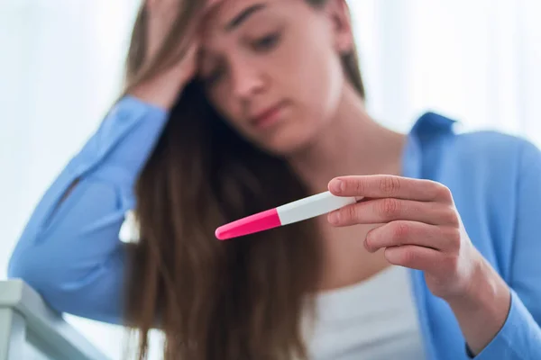 Upset sad woman holds pregnancy test with positive result. Unplanned and unwanted pregnancy