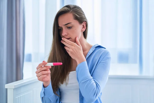 Woman surprised by positive pregnancy test result. Unwanted and unplanned pregnancy