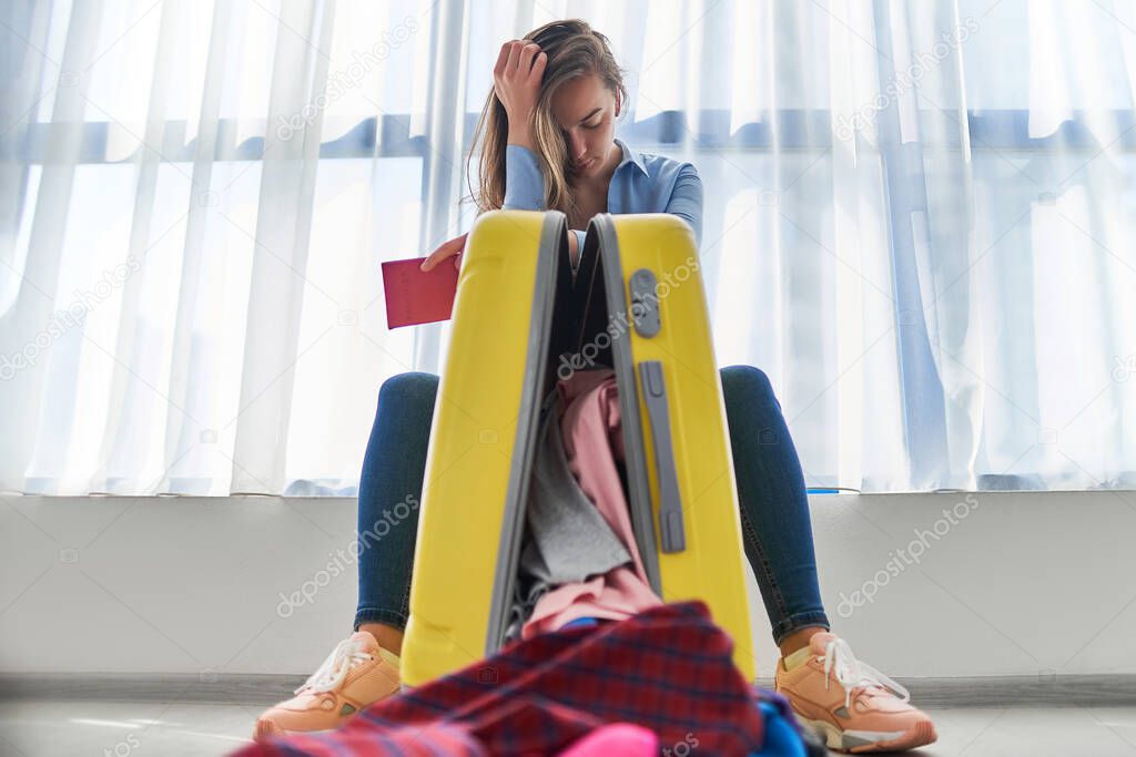 Upset woman traveler with yellow suitcase affected by flight delay and cancelled travel and vacation weekends holiday. Travel ban and traveling troubles 