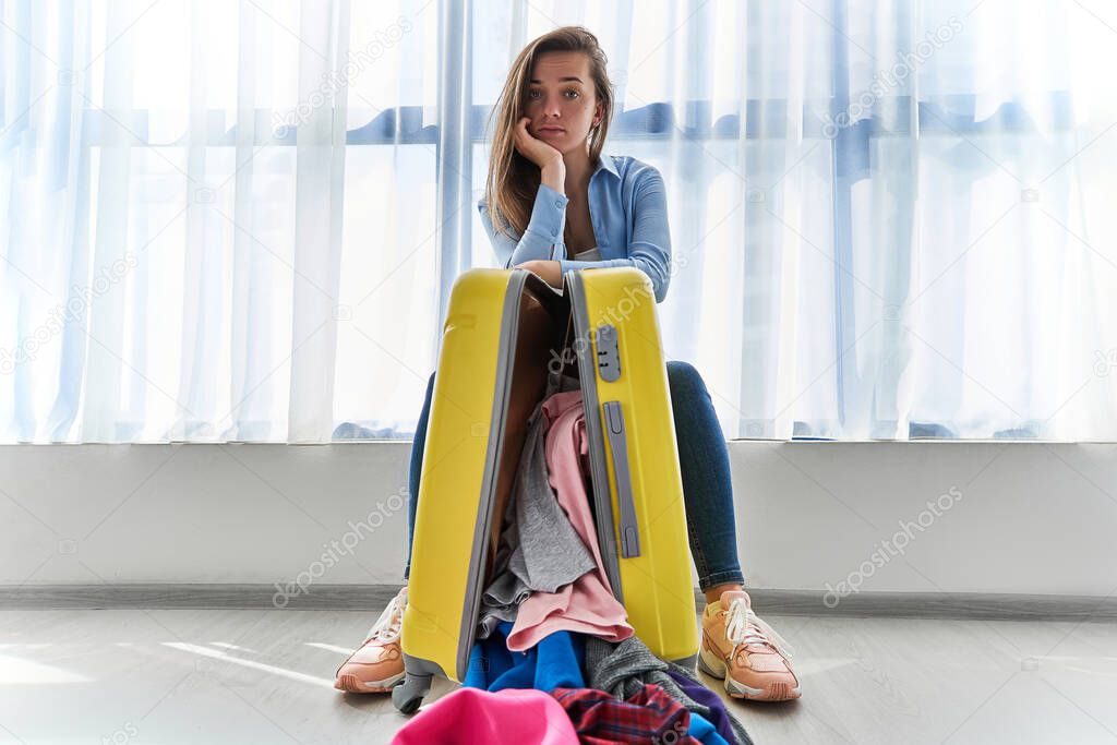 Portrait of upset woman traveler with yellow suitccase affected by flight delay and cancelled travel and vacation. Travel ban and traveling troubles 