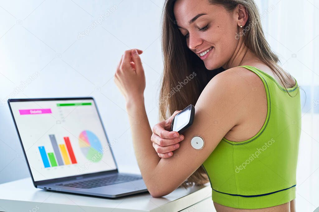 Woman diabetics using remote sensor and computer for control, online monitoring and examining glucose blood levels graphs. Diabetes lifestyle 