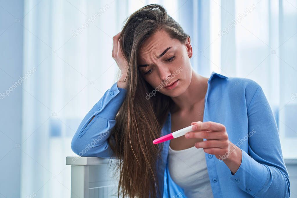 Sad upset unhappy woman holds pregnancy test 