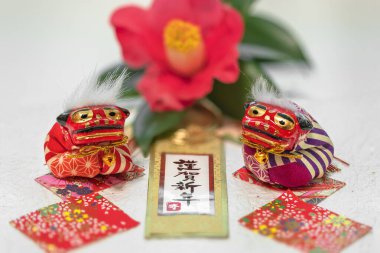 El yazısı ideogramları olan Japon Yeni Yıl Kartı Kingashinnen ya da Mutlu Yıllar ve arka planda bir tsubaki kamelyası çiçeğine karşı iki Shishi aslanı.