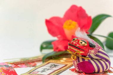 Japon Yeni Yıl Kartı 'nda bir Shishi aslan heykelciğine karşı bir tsubaki kamelya çiçeği ve Kingashinnen sözcüğü var..
