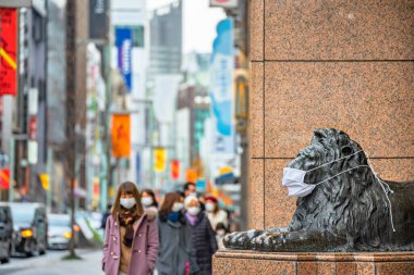 Tokyo, Japonya - Ocak 08 2021: Aslan bronz heykelinin yanında yürüyen bir yaya, Ginza 'daki salgın sırasında Mitsukoshi mağazasının giriş kapısında maske takıyor..