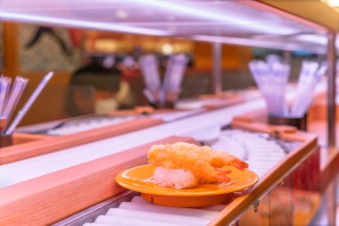 Japonya 'da bir taşıma bandı suşisinde ya da Kaiten-zushi restoranında iki parça tempura karides suşisi taşıyan bir tabağa yaklaş..