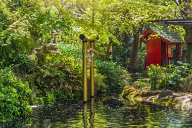 Tokyo, Japonya - 13 Nisan 2020: Altın torii kapısı Atago Tapınağı 'nın yukarısındaki akçaağaç ağaçlarının altında bir shimenawa ipiyle süslenmiş ve arka planda tanrıça Benzaiten' e adanmış bir Massha türbesi var..