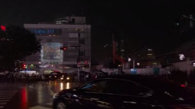 Tokyo, Japonya - 25 Ekim 2019: JR Shinjuku Doğu İstasyonu Meydanı kavşağında sağdaki otomobil ve turist otobüsü videosu yağmurdan ıslanmış ve gece aydınlık gökdelenleri yansıtıyor.