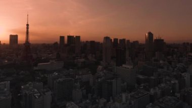 Tokyo, Japonya - 10 Mayıs 2021: Tokyo 'nun Daimon ilçesinin Tokyo kulesi ve Roppongi Hills gökdelenlerinin arkasında gün batımı gökyüzü olan şehir manzarasının Pan videosu.