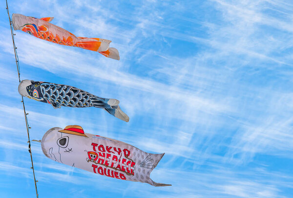 tokyo, japan - may 05 2021: Close up on Japanese Koinobori or carp streamers on the Tokyo Tower and adorned with logo of the Tokyo One Piece Tower amusement park against a cirrus clouds background.