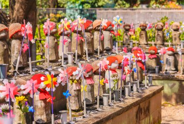 tokyo, japan - april 06 2021: Thousand statues of Kosodate Jizo bodhisattva protector of children wearing a red knit cap with a baby bib and adorned with pinwheels in the Buddhist Zojoji temple.