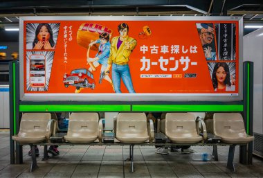 Tokyo, Shinjuku - Bölüm 22 2025: Japon tren istasyonunda boş sandalyeler ve Araba Sensörü Şehir Avcısı için büyük bir reklam kullanılmış araba arama çalışmalarını desteklemek için manga karakterleri.