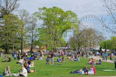 İnsanlar 24 Nisan 2021 'de Stratford-upon-Avon' daki dönme dolaba bakan çimlerin üzerinde dinleniyorlar.