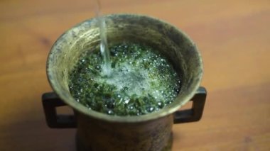 Bakır bir kaseye su dök, şifalı bir bitkiyle bitkisel bir tentür oluşturur.