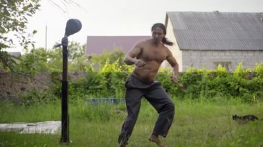 Doğulu bir adam, uzun siyah saçları ve güzel bir gövdesi var, annemi bahçede çalıştırıyor, tekme çalışıyor, tekme atıyor, ön tekme atıyor.