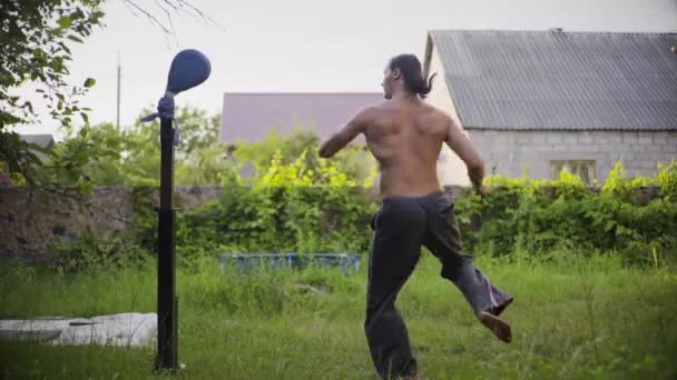 Tipo atlético con pelo negro largo y un hermoso torso, practicando taekwondo en el jardín, practicando patadas — Vídeos de Stock