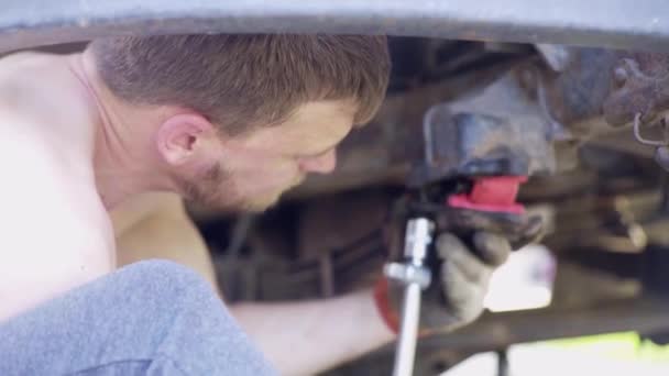 Cara repara um carro velho, muda amortecedores, close-up, cara fica debaixo de um caminhão — Vídeo de Stock