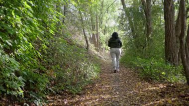 Yaşlı bir kadın orman yolunda koşuyor, sabah koşusu yaparak sağlıklı bir hayat sürüyor. Canlı sonbahar yapraklarıyla kaplı manzaralı bir yolda huzurlu ve sakin bir şekilde yürümekten zevk alıyor..