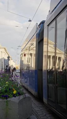 Tramvay, tarihi binalar ve çiçek açan çiçeklerle çerçevelenmiş hareketli bir şehir caddesinde süzülüyor.