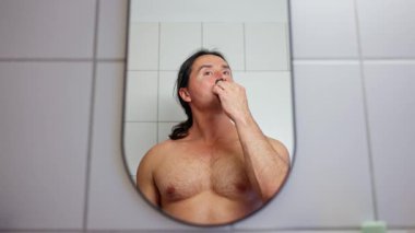Bir adam banyo aynasının önünde günlük bakım alışkanlıklarını sergileyerek kendini tımar ederken görülüyor. Yüksek kalite 4k görüntü