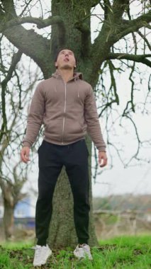 Sakin bir birey açık havada dikkatli nefes alıyor, doğal kırsal alanda meditasyon yapıyor, Asyalı bir adam açık kırsal kesimde yapraksız ağacın altında sessizce duruyor.