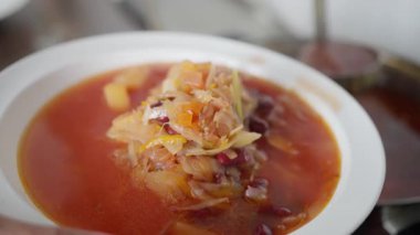 Beyaz bir tabak lezzetli çorba, taze malzemelerle yavaşça kaynıyor, gerçek aşçılık sanatı sergiliyor. Ukrayna çorbası. Ağır çekim. Yüksek kalite 4k görüntü