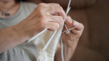 İki uçlu iğnelere beyaz çorap ören elleri kapatın, yavaş ritmik dikişler, yumuşak yün dokusu, sıcak oturma odası arka planı, rahat ev atmosferi, odaklanmış becerikli hareket