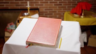 Sunak örtüsü üzerine kırmızı kitap, kurdeleli deri kapak, beyaz keten üzerine kapalı sayfalar, okutman.