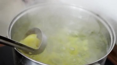 Kaynamış patates küpleri paslanmaz tencerede, buharlı kepçe yakın çekimi sobanın üzerindeki kaynayan sudan yumuşak yumru parçaları kaldırma, ellerin püre için donitlik testi, aile yemeği hazırlayan ev aşçısı