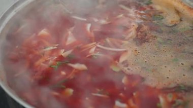 Patlamış lahanayla kaynayan domates güveci, kaynayan kırmızı et suyu ve sebzelerin yakından çekimi, kepçenin dolgun sebzeleri karıştırması ve aromatik köpük, kırsal mutfakta buhar yükselirken aşçı yemek hazırlıyor.