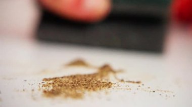 Beyaz tezgahın üstündeki siyah biber kalıntılarını silmek, desenli pedin bastırılmış olduğu yakın tutulan eylem, bloknotlar emerken granüller dağılıp yapışırken, dokunsal temizlik hareketi gerçekçi.