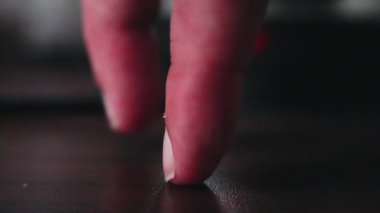 Yakın plan parmak ucu masada yürüyor. Yetişkin eli, karanlık ahşap yüzey boyunca yavaşça ilerliyor. Sıcak ortam ışığı ve yumuşak gölgesi, görünür tırnak ve deri dokusu, hafif basınç ile.