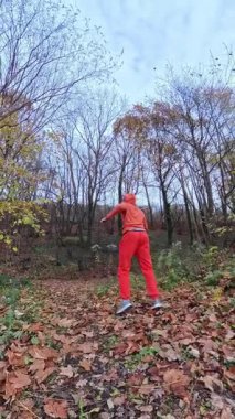 Kırmızı eşofmanlı dövüş sanatları patlayıcı tekmeleri ve çevik ayak hareketlerini bulutlu gökyüzü altında, canlı enerji altında, güçlü inişler, hızlı inişler, eğitim sekansını vurguluyor.