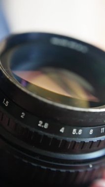 Kamera merceğindeki açıklık göstergeleri, sıcak stüdyo aydınlatma atmosferiyle aydınlatılan dokunsal metal halka, antika merceklerin odak çemberini değiştiren teknisyen, gözle görülür açıklık işaretleri.