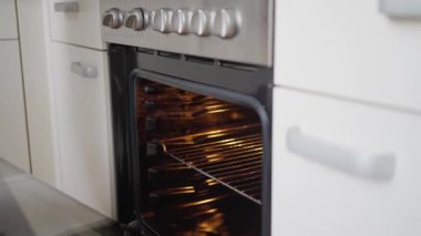 Fırında pizza, pişirme, paslanmaz çelik menzil, parlayan raflar, peynir ve sebzeler üzerine pizza, sıcak mutfak atmosferi, evde akşam yemeği hazırlığı için ellerin ısıtılmış ev fırınına sokulması.