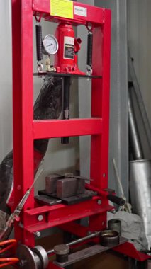 Atölyedeki kırmızı hidrolik baskı görünür basınç göstergesi ve kırmızı çerçeve ile çelik bloğu sıkıştırıyor, yakınlardaki klemp ve çalışma tezgahı, piston ve silindir montaj, ayarlama işaretleri gösterge üzerinde, operatör test işareti