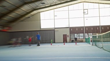 Tenis kortunda beyaz erkek antrenör koni ve öğrencilerle grup dersine rehberlik ediyor, kavrama ve yürüyüş teknikleri, destek antrenörlüğü, enerji ısınması ve ayak çalışması, kulüp,