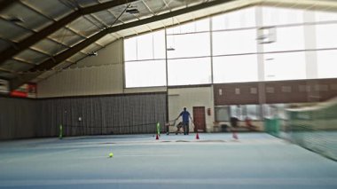 Kapalı alanda tenis oynayan erkek rakip, kapalı alanda yoğun servis tekniği sergiliyor. Dinamik tenisçi, kapalı alandaki yoğun antrenman seansında kafasının üstünde raket uzatıyor. Yavaş çekim