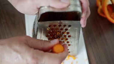 Metal kutuda havuç ızgarası yapan eller. Orange Shreds 'in tabaklara düştüğü sessiz mutfak sahnesi, dikkatli parmak ucu tutuşu, salata veya garnitür için ev tarzı hazırlık..