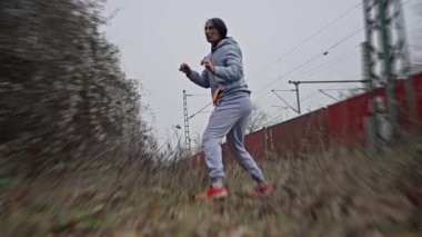 Siyah adam gölge boksu ve tren konteynırlarının yanında pratik yapma, soğuk bulutlu aydınlıkta kapüşonlu antrenman, ritmik ayak sesleri, uzun solunum ve çiğ endüstriyel atmosfer...