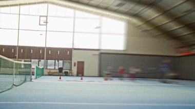 Hareketli Bulanık Oyuncuların Çeviklik Konileri 'nde koştuğu kapalı tenis kortu, Hızlı Çocuk Tatbikatları ve Koç Whistles, Parlak Üst Pencere ve Yüksek Enerji Uygulaması, Mavi Yüzey