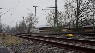 Gri Gök 'ün Altında Uzak Ufuk' a uzanan Sinyal, Boş Demiryolu Rayları, Tepe Kabloları, Çelik Sütunlar Yapraksız Ağaçlar ve Küçük Banliyö Evleri ile Bulutlu Kırsal Demiryolu Rayları. 4k görüntü