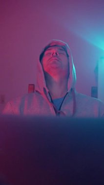 Bir gecede Laptop 'ta Kapüşonlu Adam, Yorgun İfadeler, Arkaya yaslanmış Gözler Kapalı, Neon Pembe ve Cyan Parıltısı, İçişleri Bakanlığı Yalnızlığı, Gece Finans İzleyicisi, Yorgunluk İç Çekişi, Kulaklık